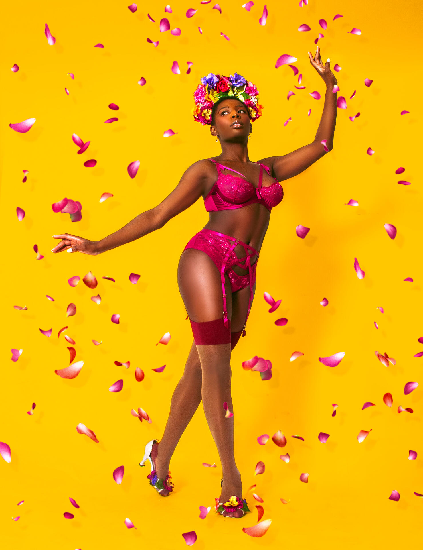 Red Tongued Raven wearing Dita Von Teese magenta lingerie against a yellow background with petals falling around her